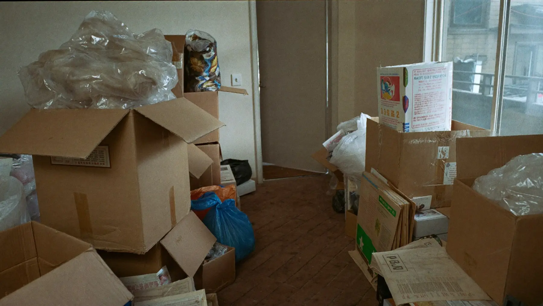 A domestic room densely packed with stacked boxes, bags and belongings leaving only a narrow path