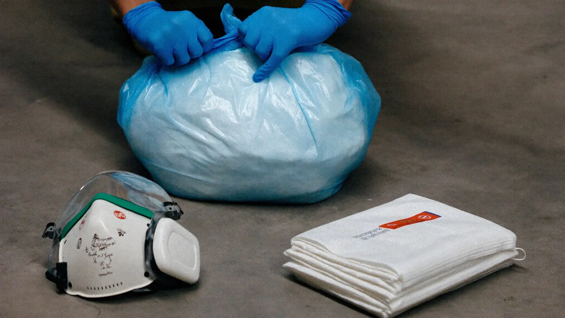 Hospital grade disinfectant, protective equipment and sealed waste bags arranged on a plain floor
